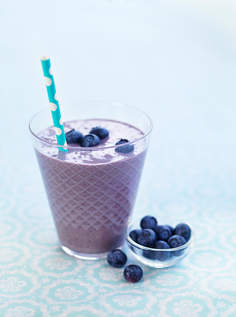 A blueberry smoothie with a straw in a glass