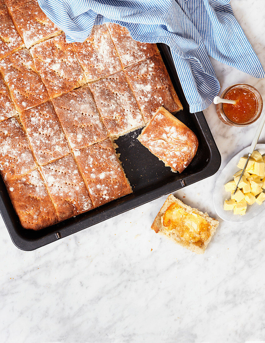 Homebaked bread on a baking sheet with butter and orange marmalade