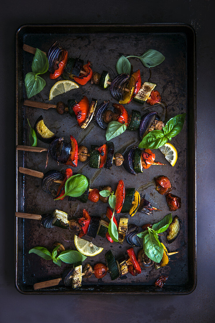 Vegetables kebabs on a baking tray with fresh basil and lemon