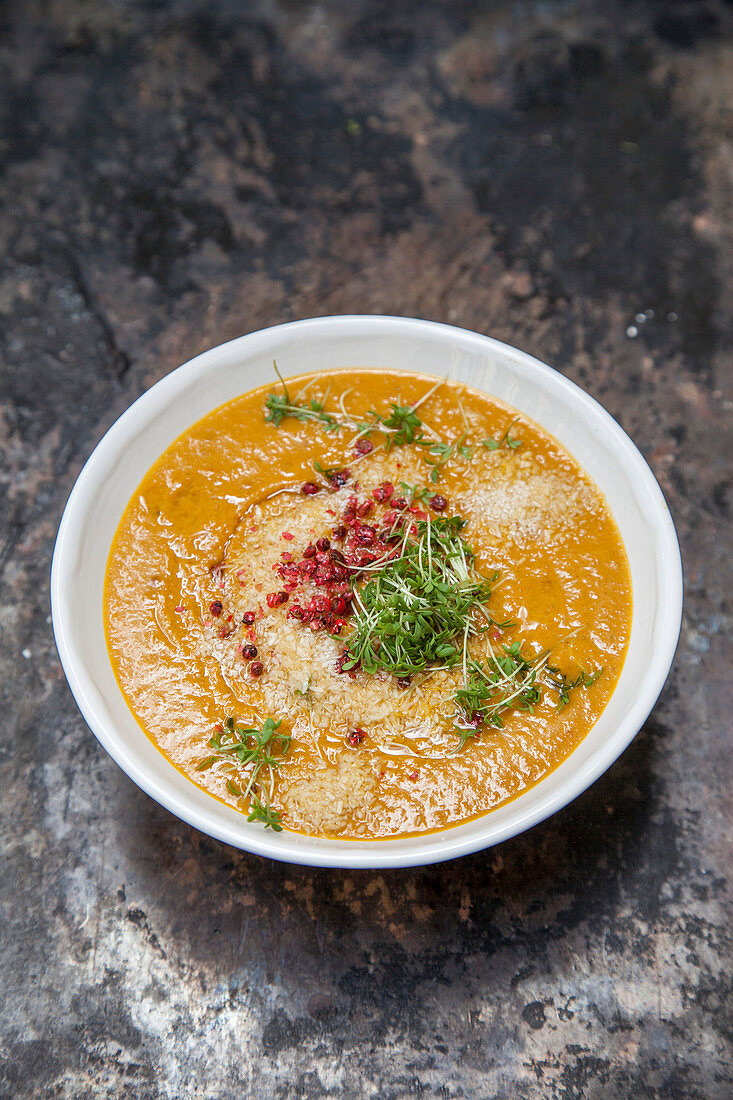 Carrot and sweet potato soup with grated coconut, red pepper and cress