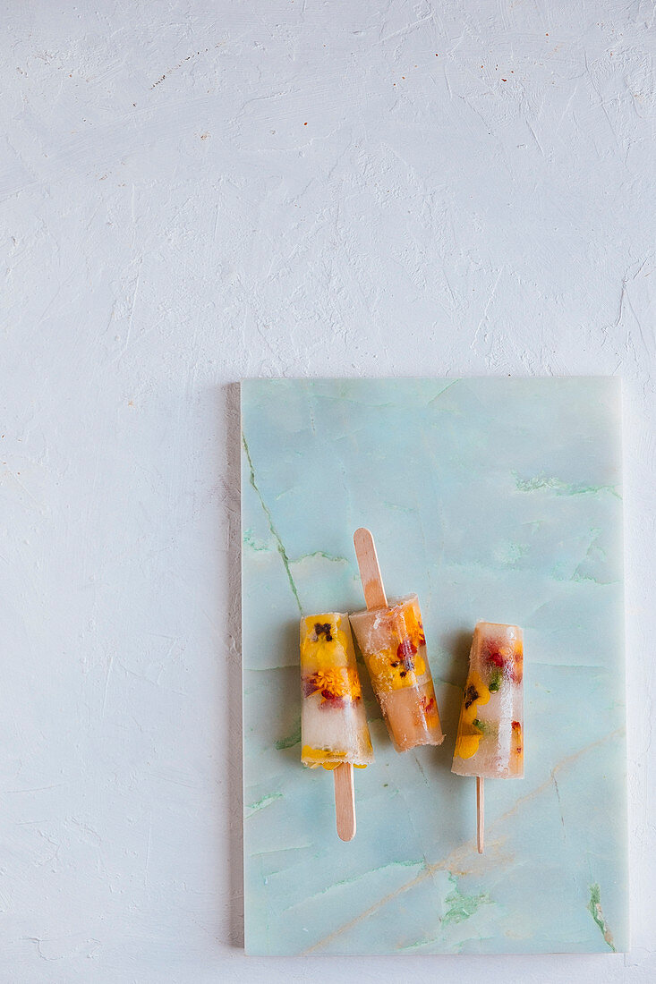 Water icecreams with elderflower syrup and eatable flowers on a marble plank and a white backdrop