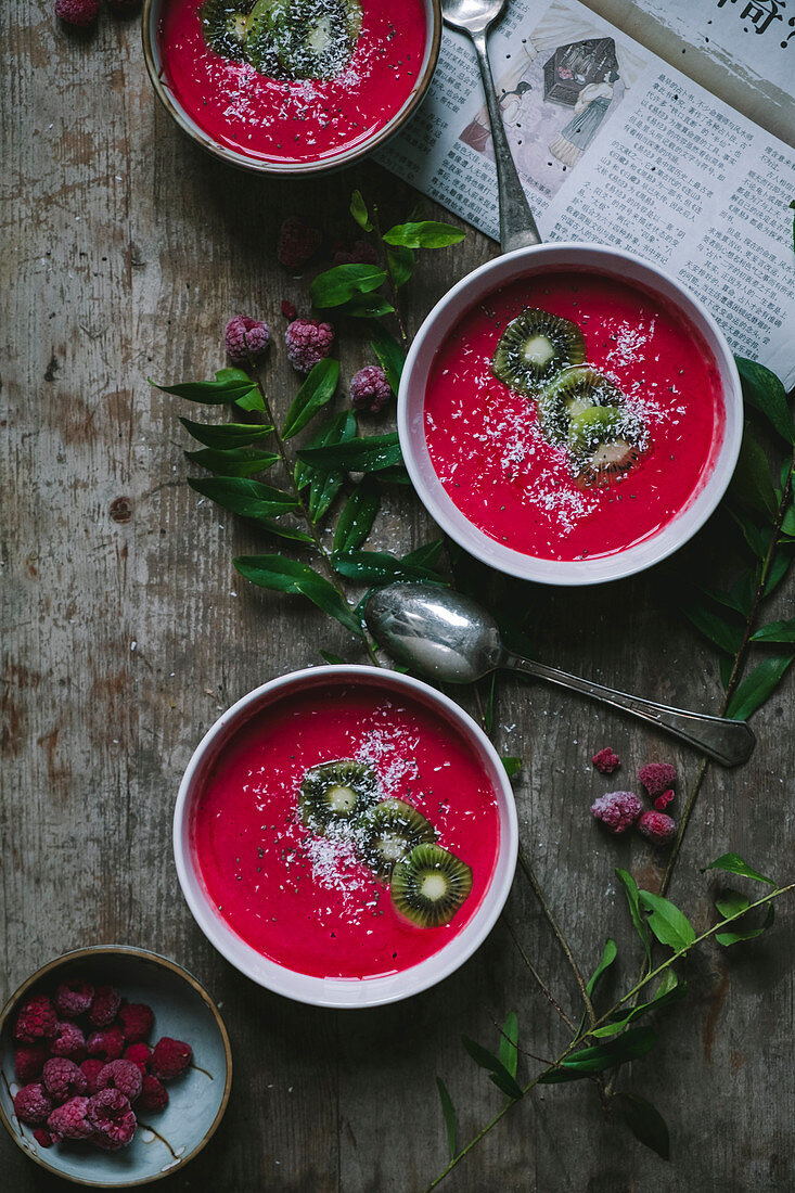 Raspberries smoothies in three bowls on a wooden table with a newspaper