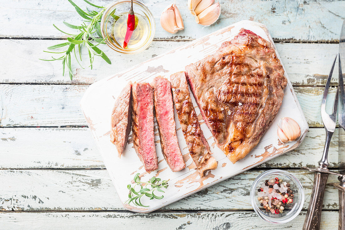 Sliced medium rare grilled beef steak on rustic cutting board with rosemary and spices, white rustic background
