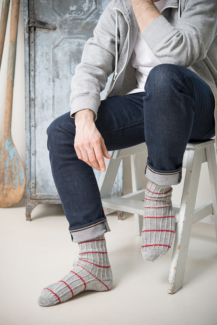 A man wearing self-knitted sock with a structured pattern and red stripes