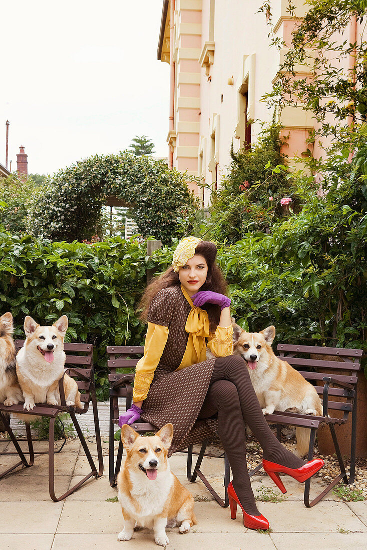 A dark-haired woman wearing a brown dress sitting on a bench with dogs