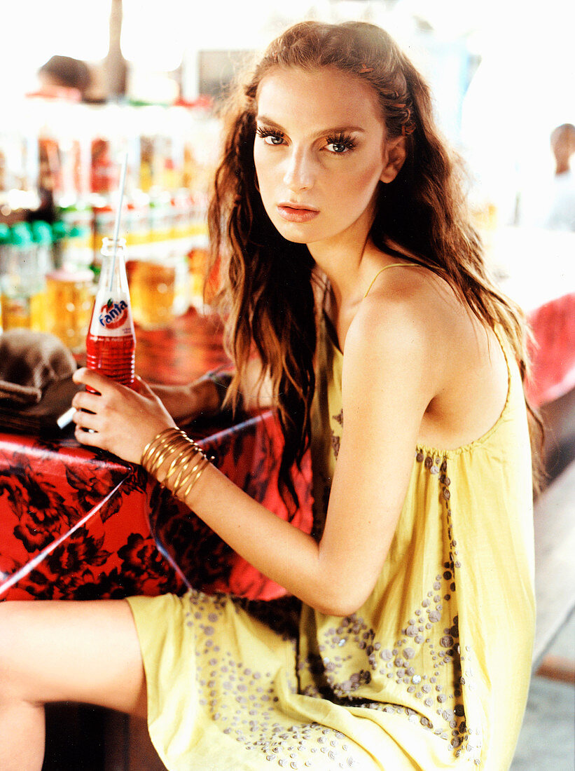 A brunette woman wearing a summer dress sitting a bar with a drink