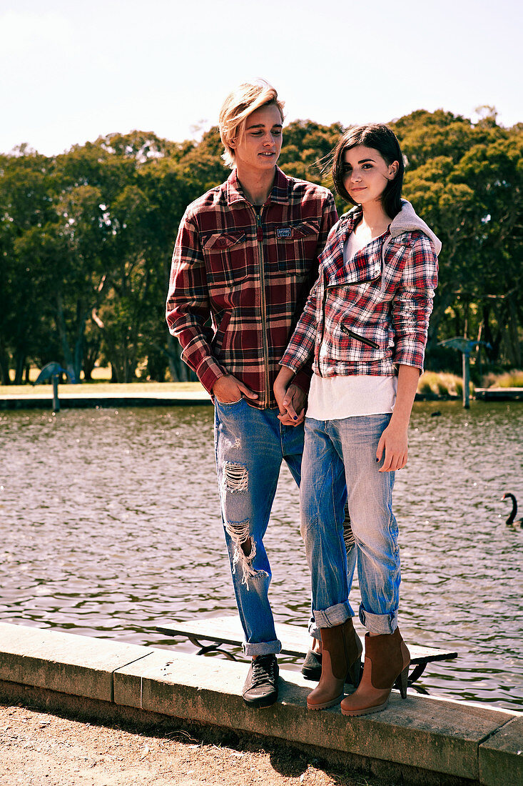 A young couple wearing matching outfits (checked shirts and jeans) standing by a river