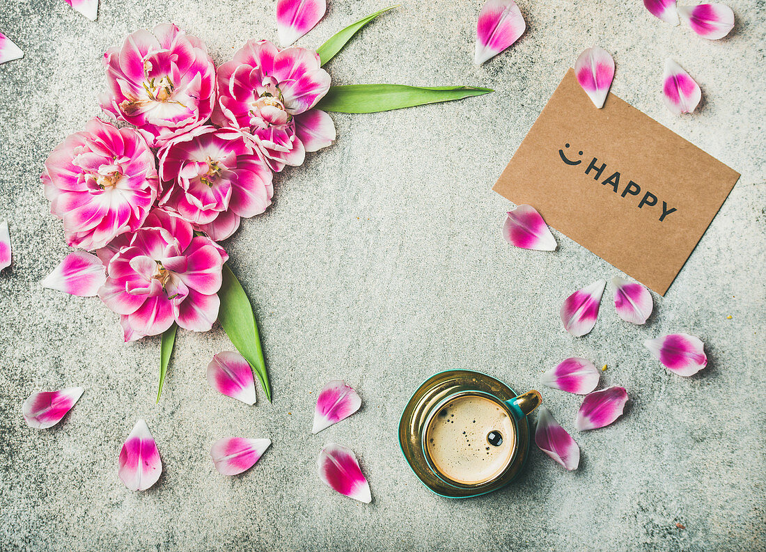 Tasse Kaffee daneben rosa Tulpenblüten und -blätter sowie Schild mit Aufschrift 'Happy'