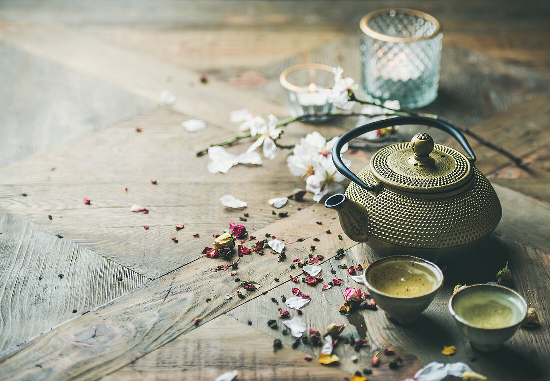 Traditional Asian tea ceremony arrangement with iron teapot, cups, dried rose buds and candles