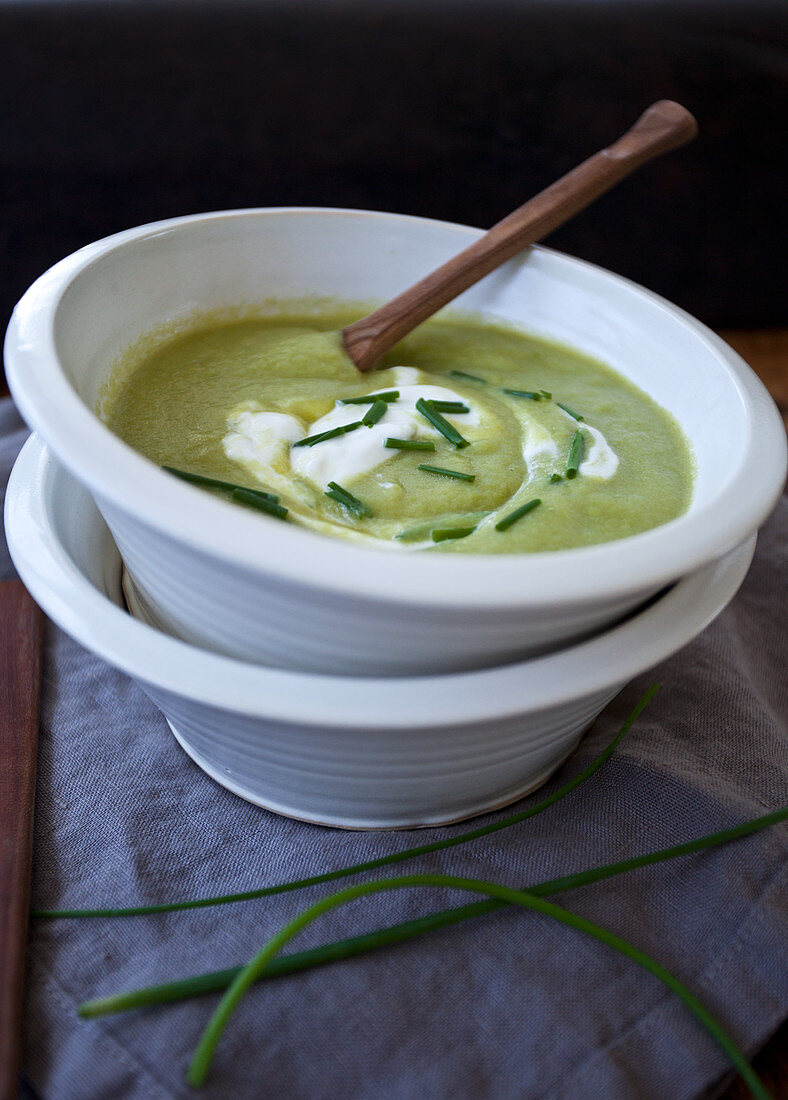 Two bowls stacked, one with asparagus soup, topped with creme fraiche and chopped chives