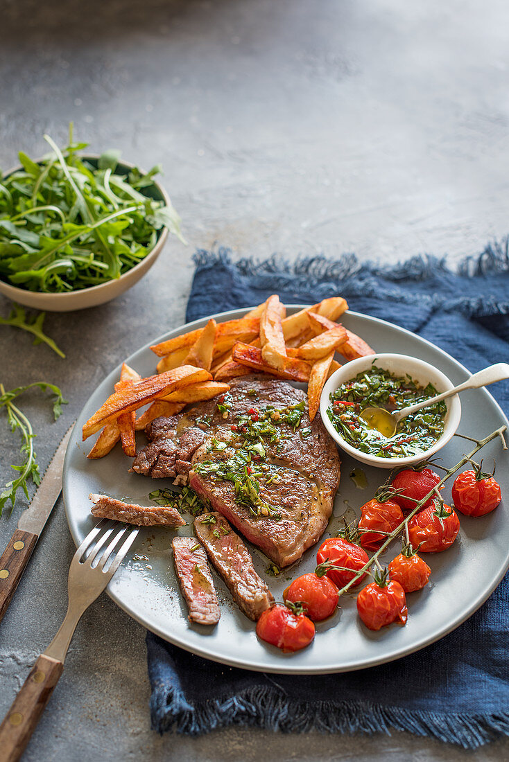 Steak with chimichurri sauce, chips, rocket and grilled tomatoes