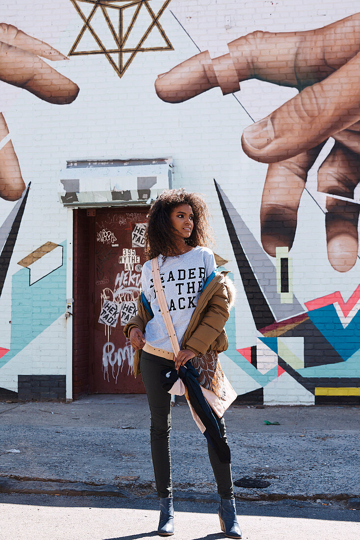 Dunkelhaarige Frau in T-Shirt, Jeans und Jacke vor Wand mit Street Art
