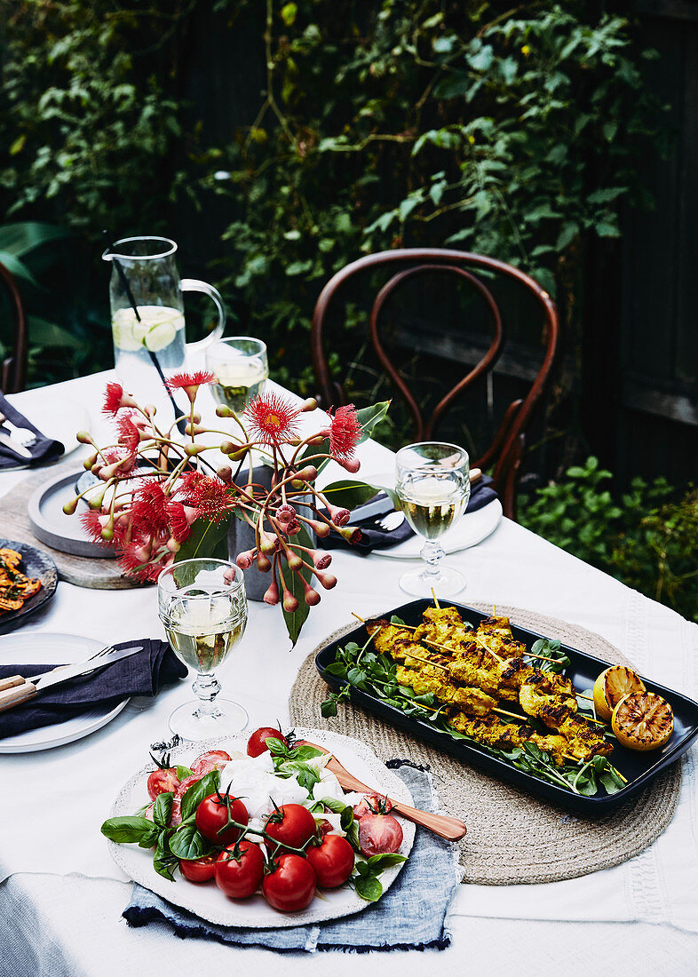 Caprese und Hähnchenspiesse auf gedecktem Tisch im sommerlichen Garten