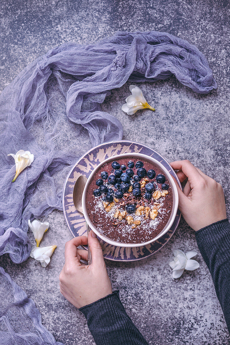 Woman eating blueberry smoothie bowl topped with blueberries, walnuts, cacao nibs and coconut