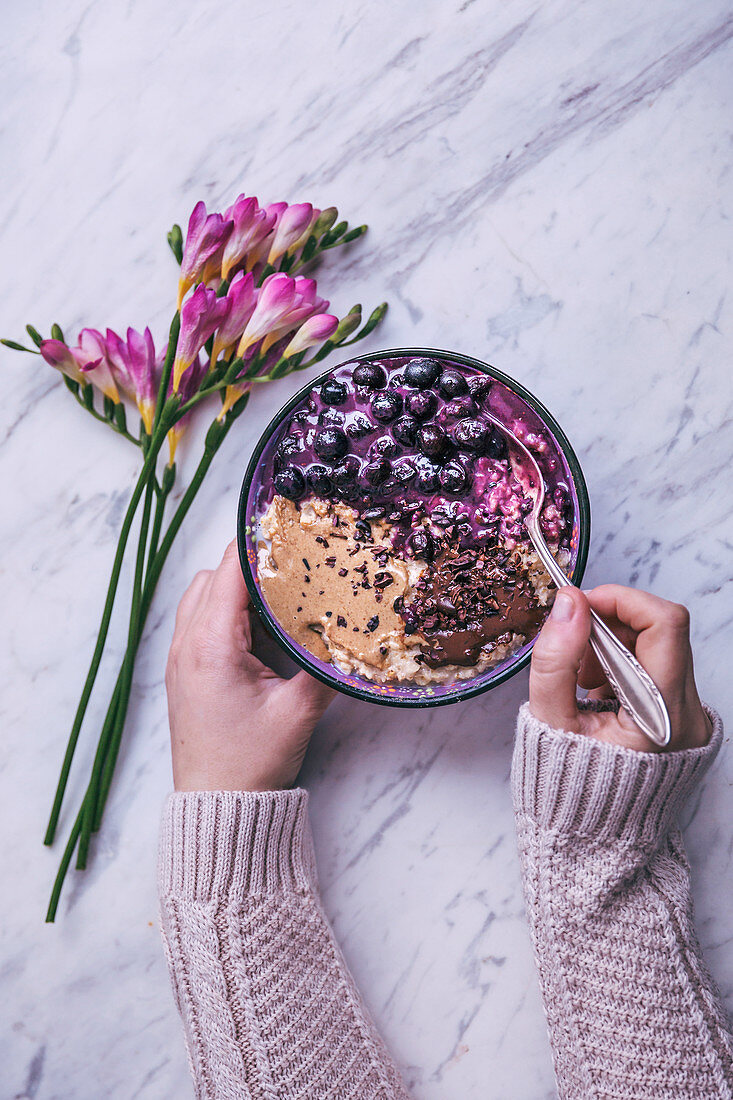 Woman eating bowl of oatmeal topped with blueberries, tahini and melted dark chocolate