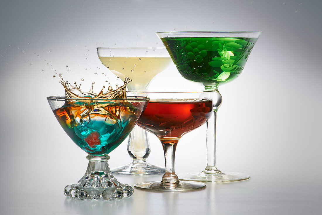 Vier verschiedene Cocktails in Gläsern vor grauem Hintergrund