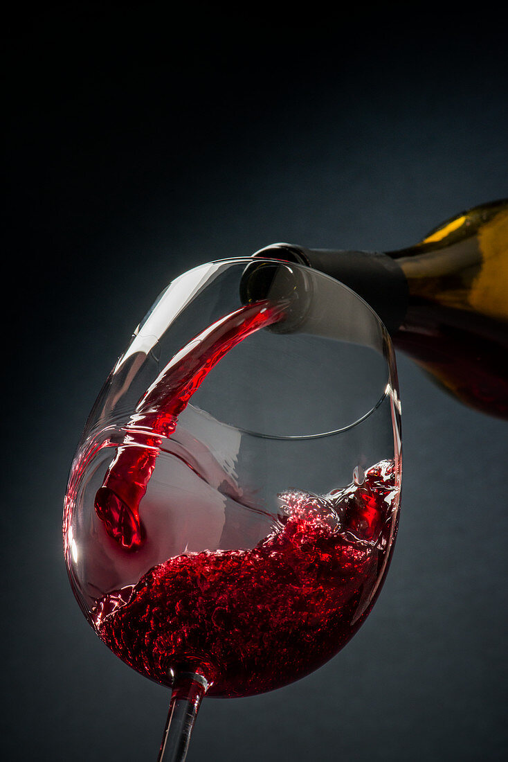 Rotwein wird aus Flasche in Glas gegossen