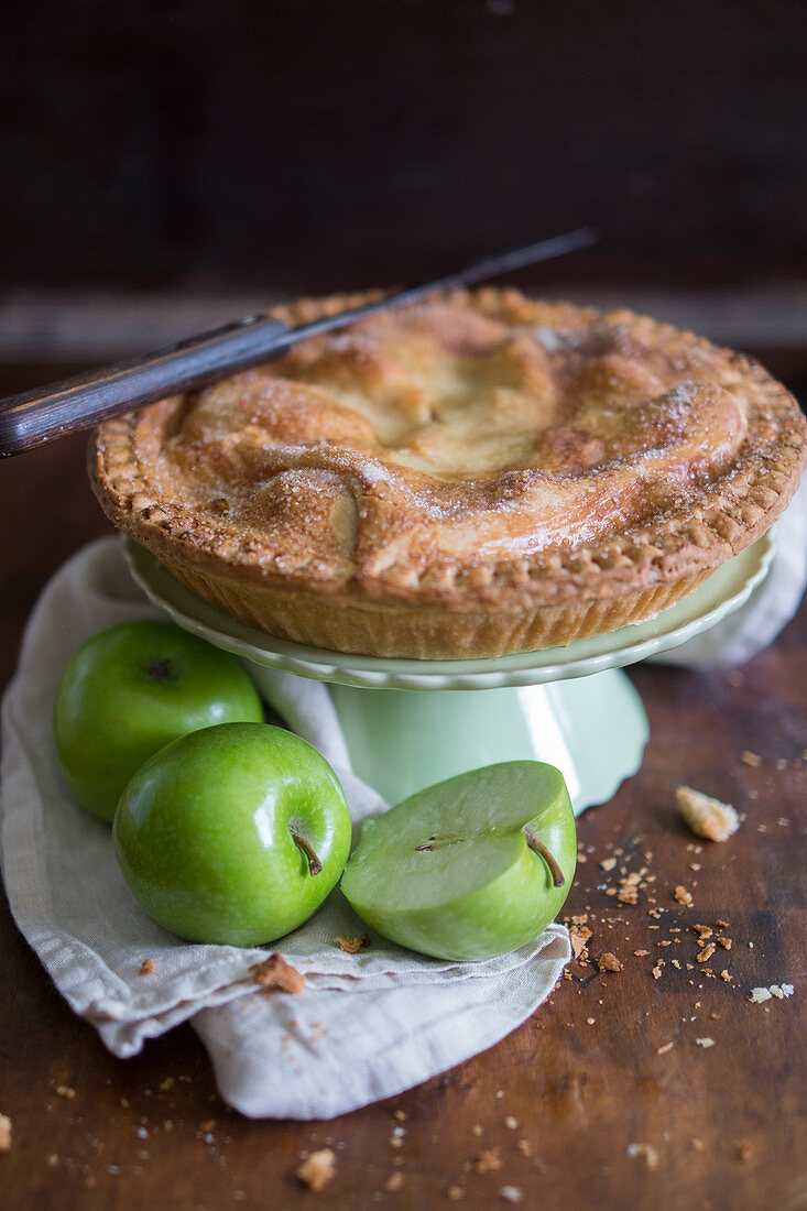Apple pie on a cake stand, and fresh green apples