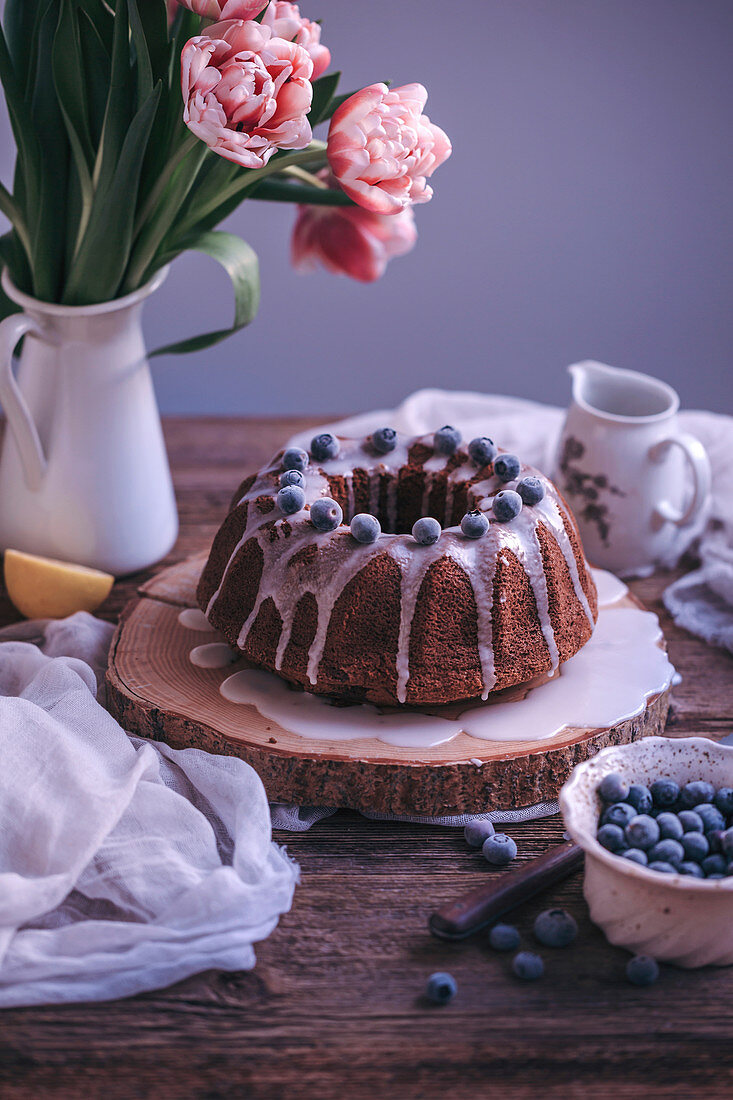 Bundt cake with lemon glaze drizzle and blueberries on a rustic wooden table