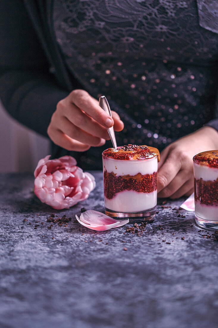 Woman eating peanut butter and raspberry chia jam parfait dessert served in a glass