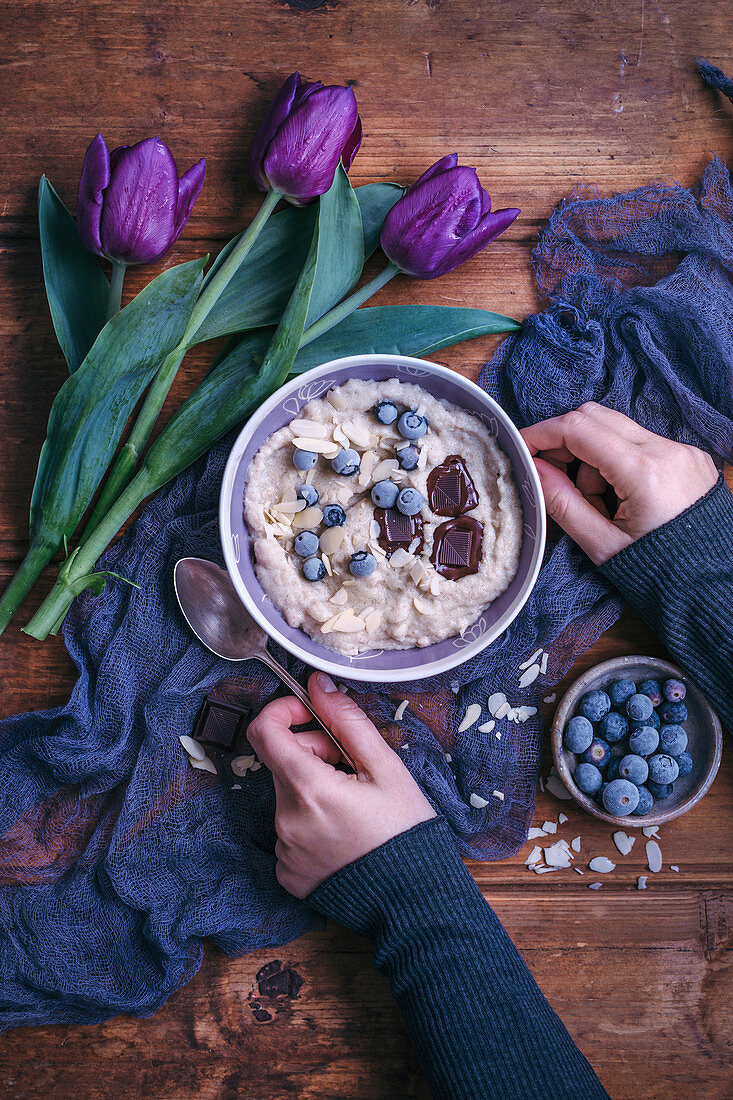 Woman eating semolina porridge topped with blueberries, chocolate and almonds