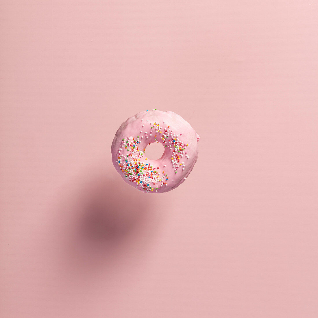 Ein rosa Donut mit Zuckerperlen, schwebend vor rosafarbenem Hintergrund