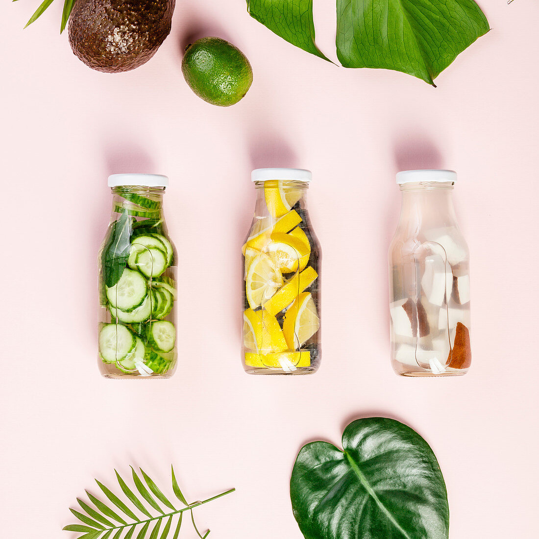 Detox fruit infused water, tropical fruits and leaves on pink pastel background
