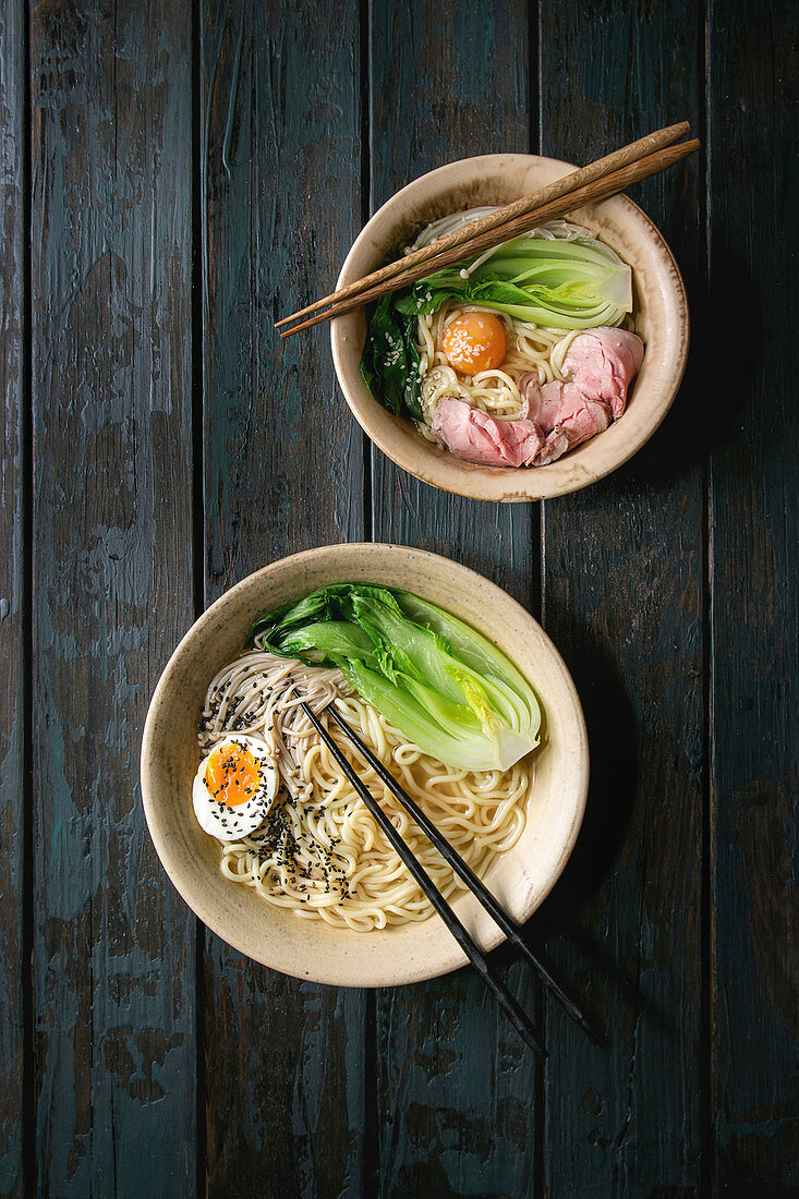 Asian dish with udon noodles with boiled egg, sesame, mushrooms, boc choy, sous vide pork meat served in ceramic bowls