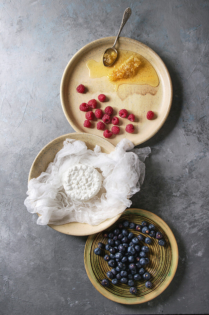 Fresh homemade cottage cheese in cheesecloth served in ceramic bowl with blueberries, raspberries and honeycombs