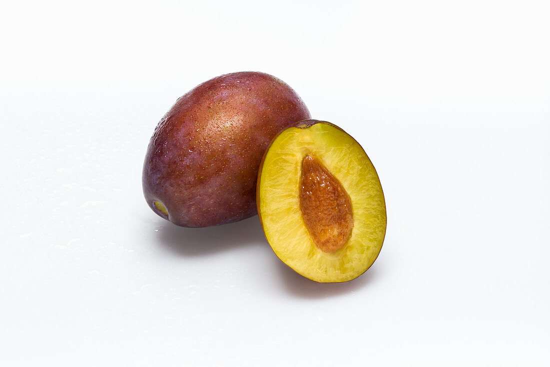 A damson and half a damson on a white surface