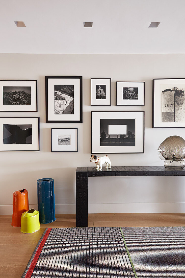 Gallery of black-and-white pictures above console table in hallway