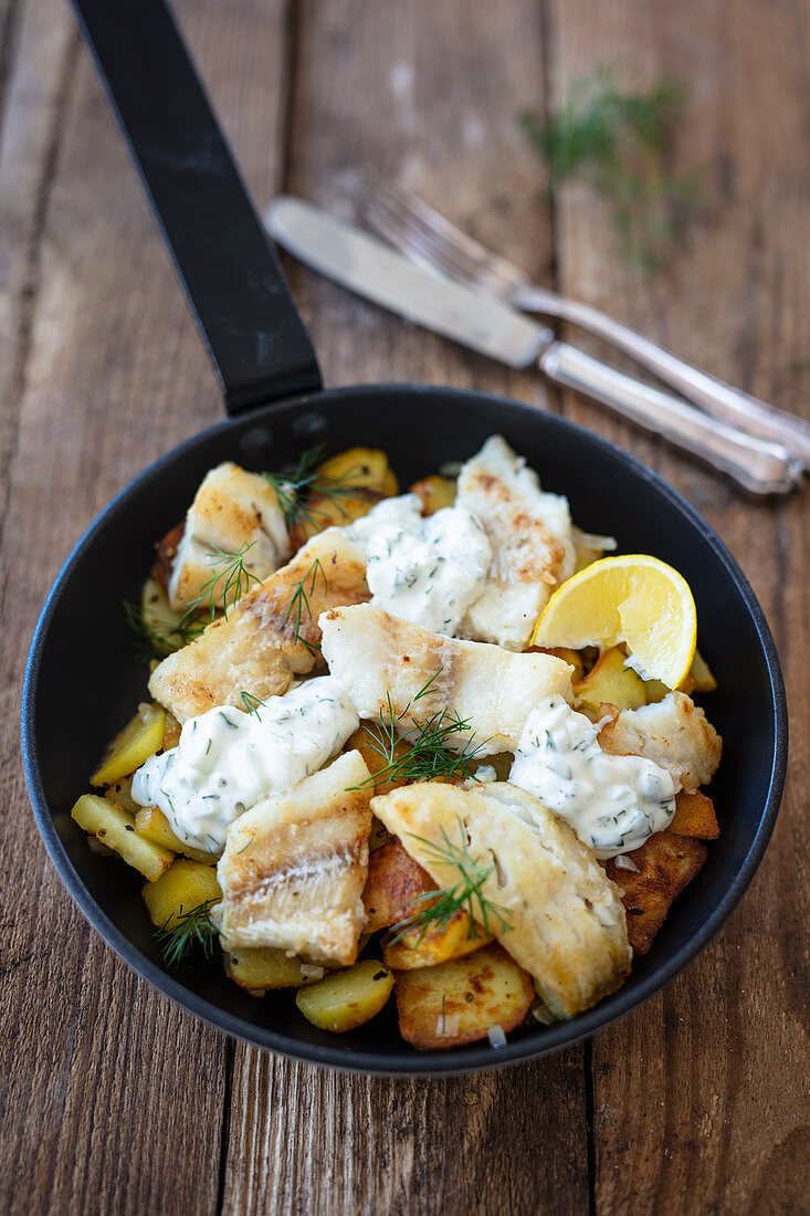 Fish fillets on fried potatoes with herb quark in a pan