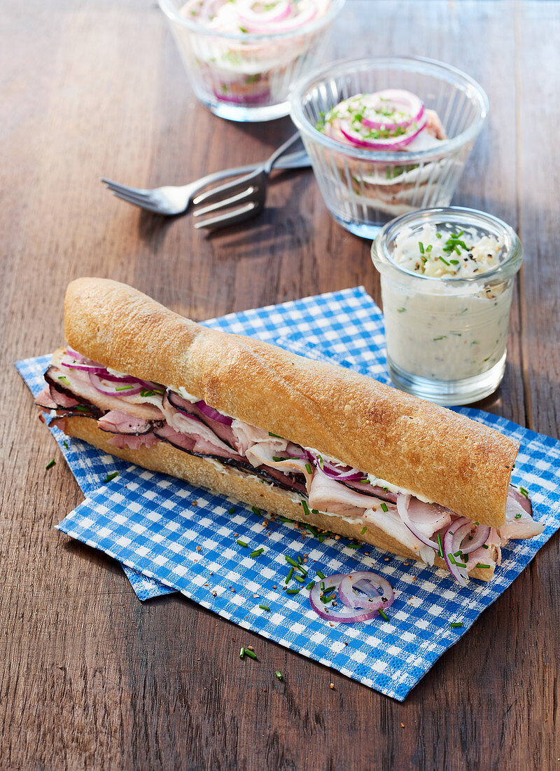 A baguette sandwich with ham, chive cream and meat salad in a jar