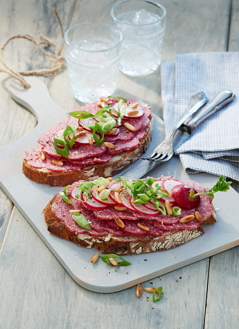 Zwei Brotscheiben mit Salami auf hellem Holzbrett