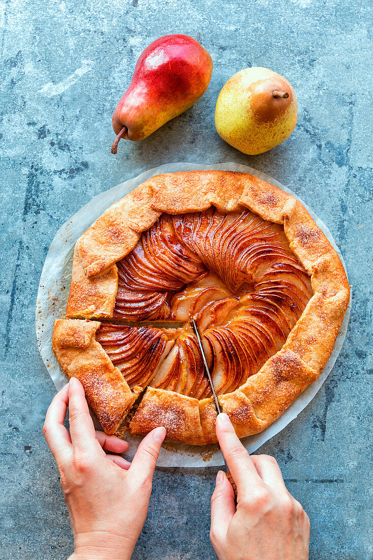 Hands cutting freshly baked pear galette