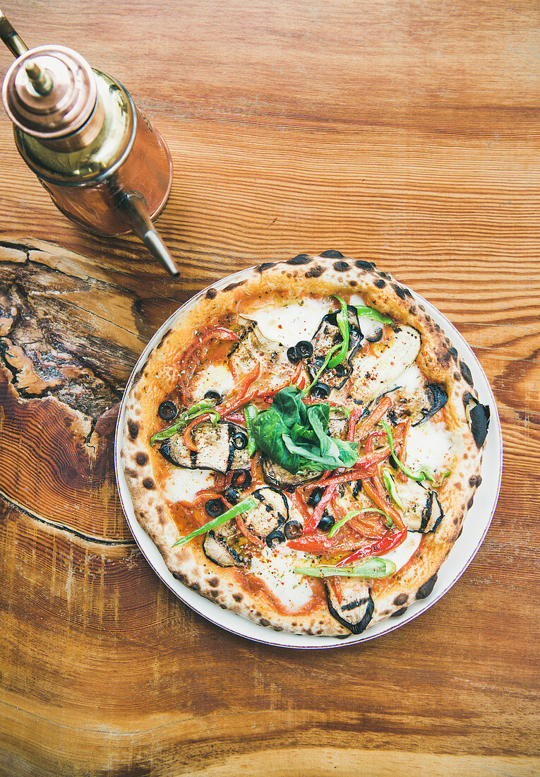 Freshly baked Italian vegetarian pizza with vegetables and fresh basil and teapot over rustic wooden background