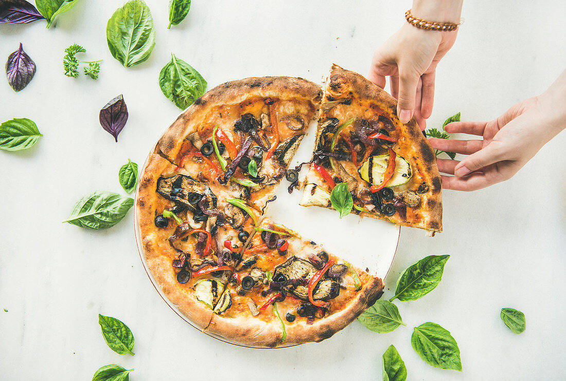 Hände greifen ein Stück vegetarische Gemüsepizza