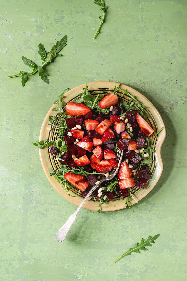 Rote-Bete-Salat mit Erdbeeren und Rucola auf Teller vor grünem Hintergrund