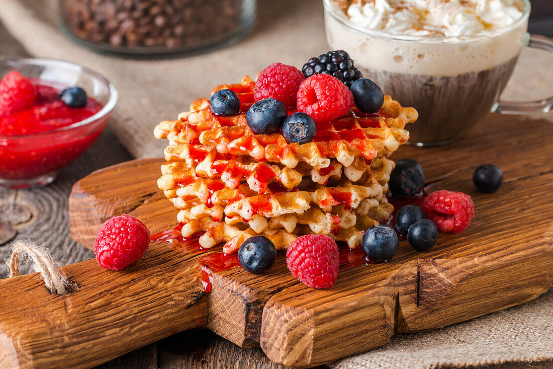 Belgian waffles with fresh berries and coffee on cutting board on rustic wooden background