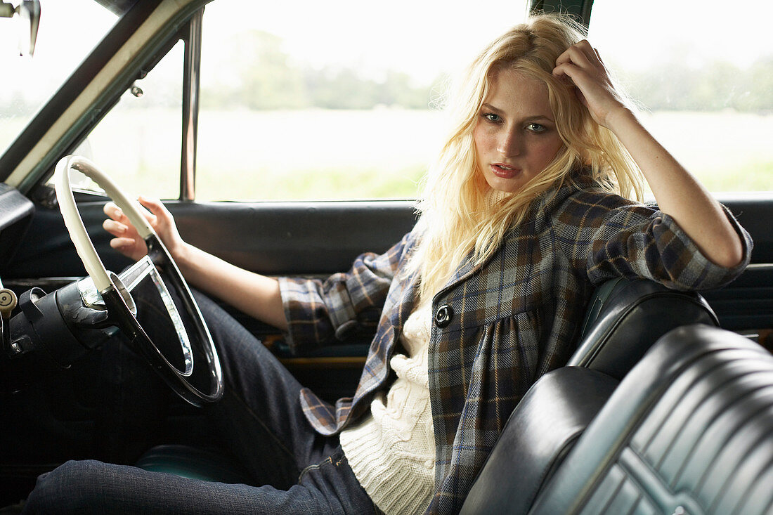 A young woman wearing a checked jacket, a jumper and jeans in a car