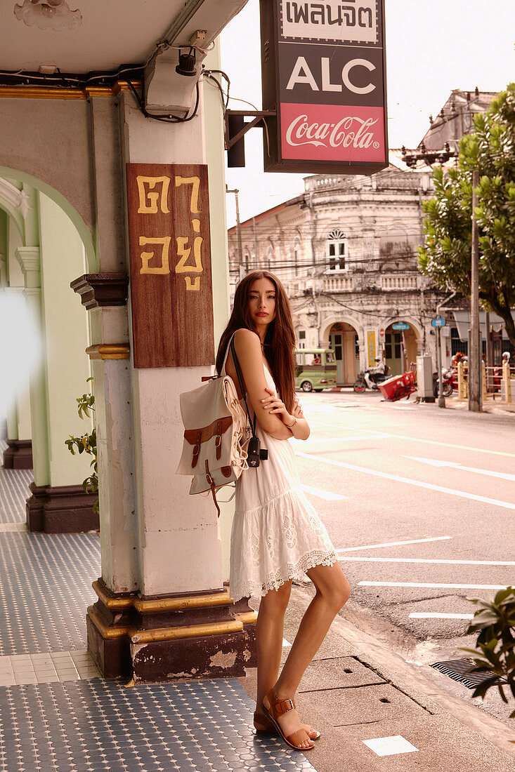 A brunette woman wearing a white summer dress with a backpack