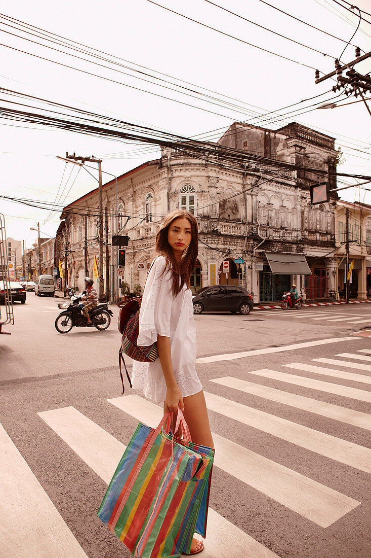 A young woman wearing a white tunic dress with shopping bags