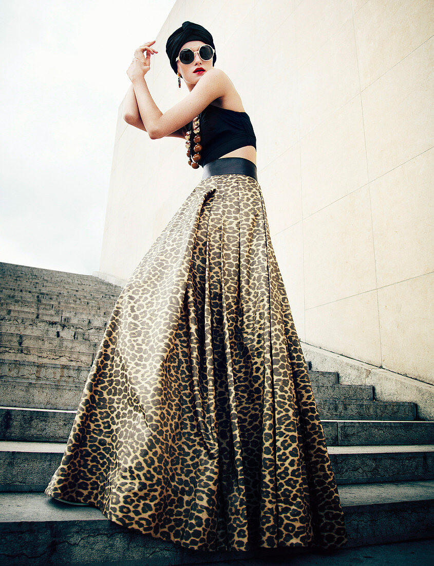 A young woman wearing a black turban, sunglasses, a crop-top and a leopard print maxi skirt