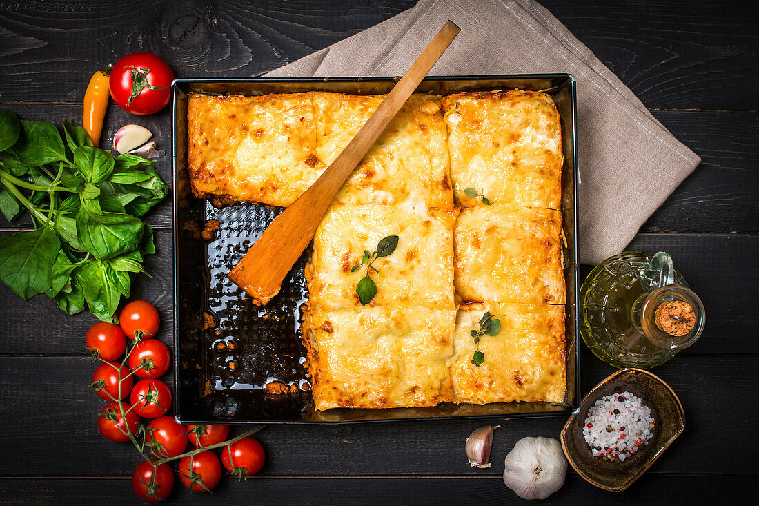 Delicious traditional italian lasagna with ingredients served on dark rustic wooden table, top view