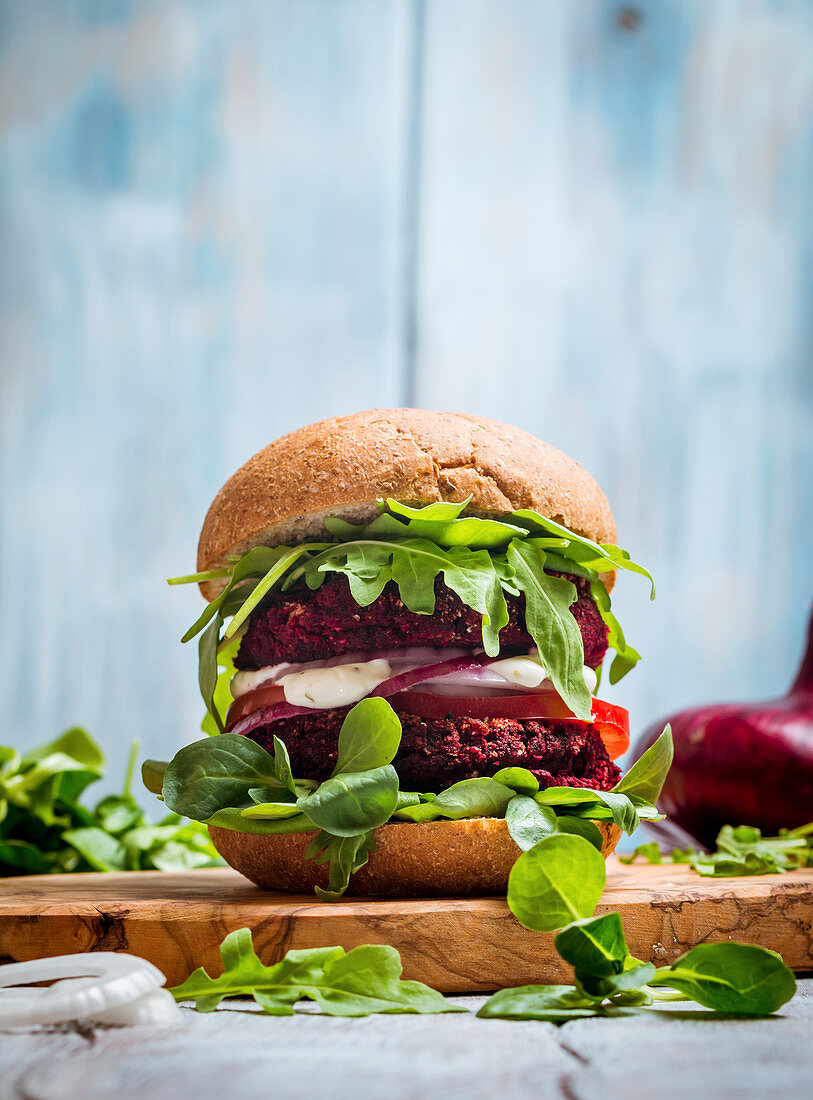 Vegetarian burger made of beetroot, tomato, corn salad and arugula on wooden background