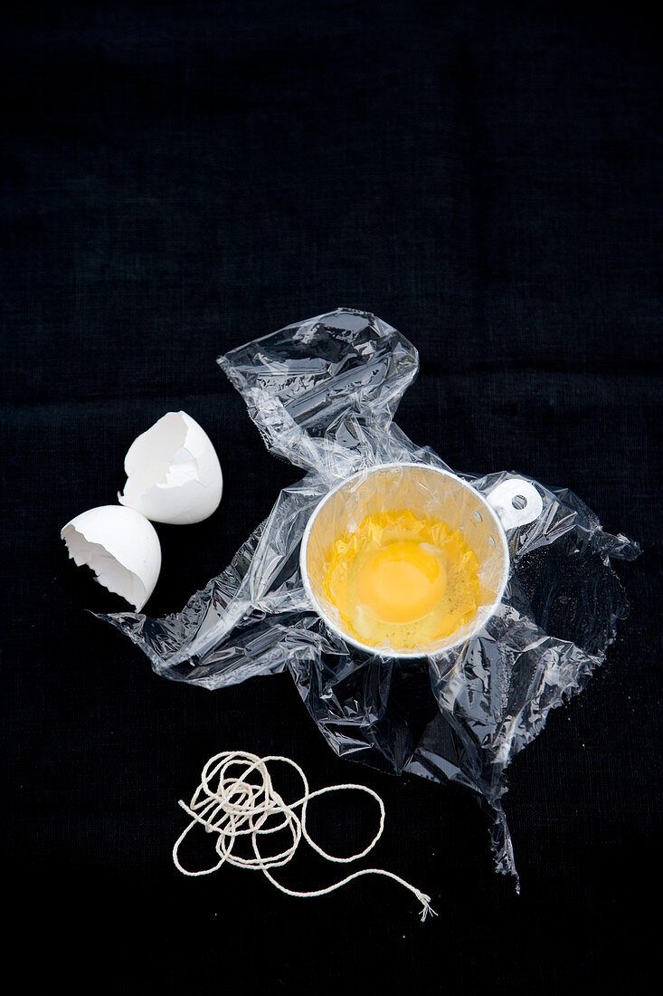 Eggs with clingfilm being poached in a cup