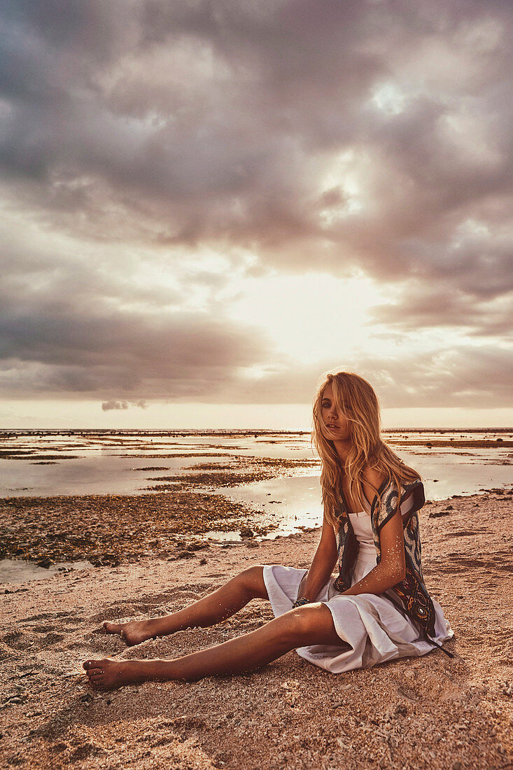 A blonde woman wearing a white dress and a waistcoat on a beach