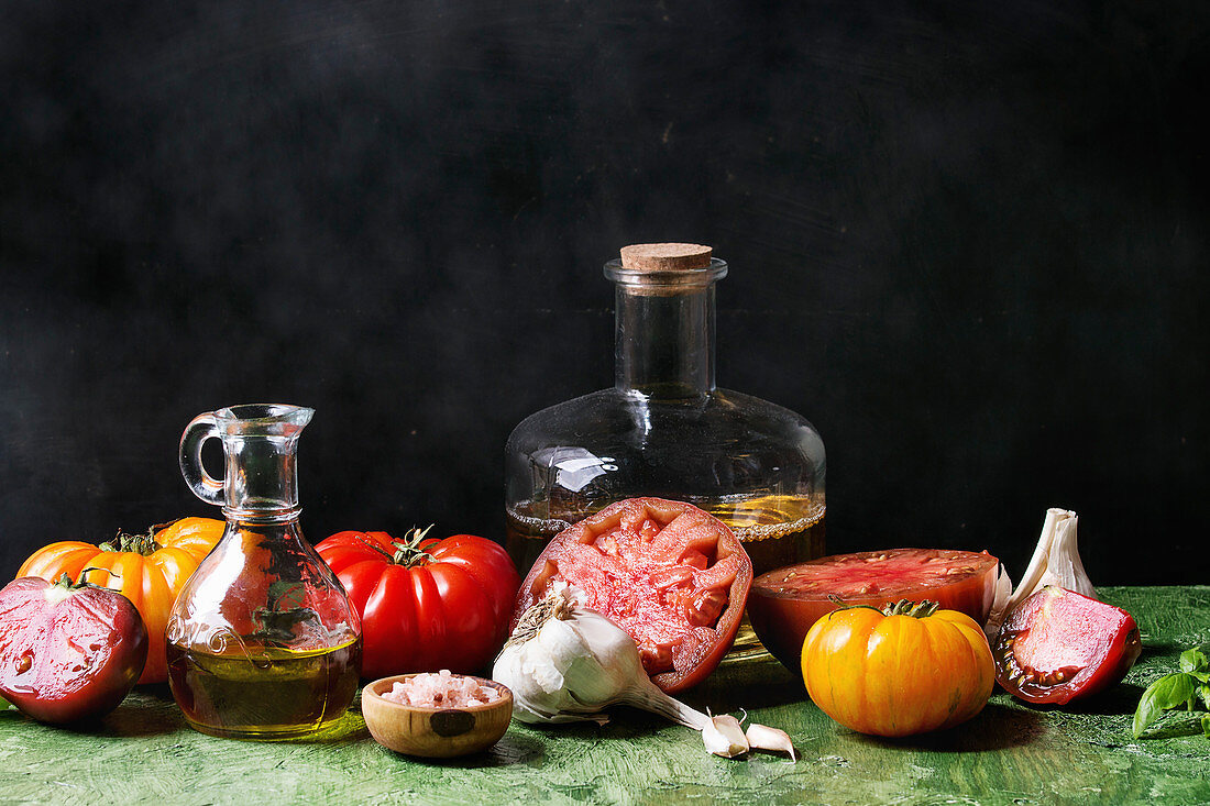 Still life with variety of red and yellow organic tomatoes with olive oil, garlic, salt for salad over green table with black background