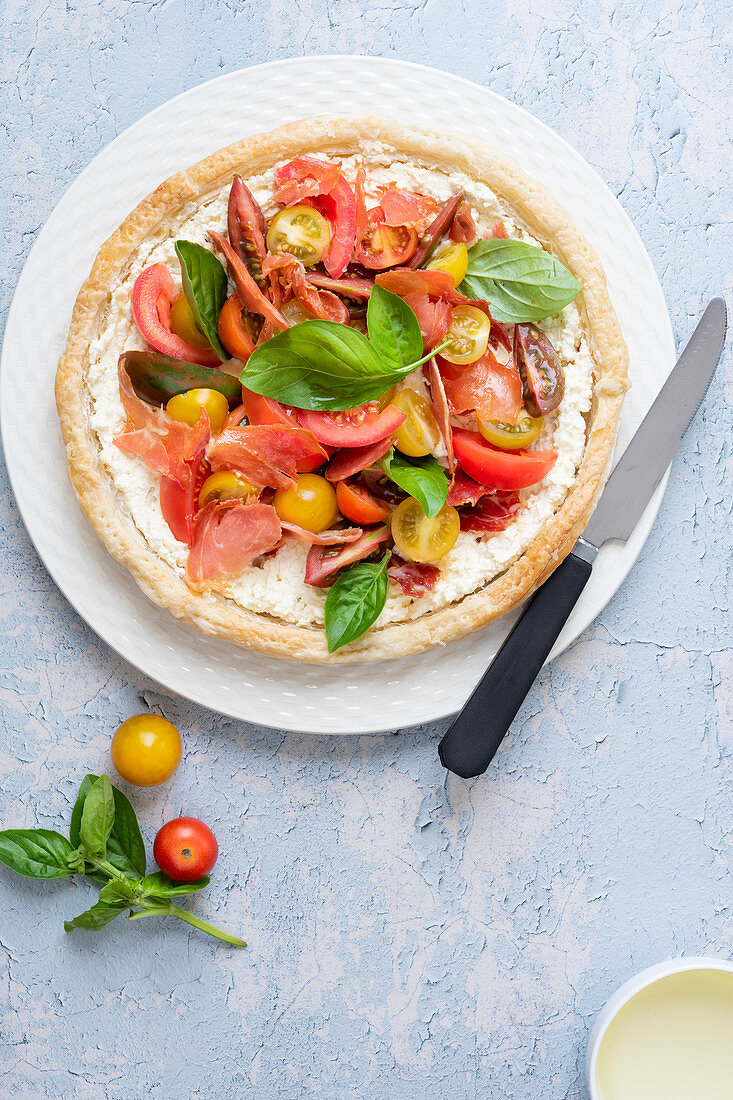 Round tart filled with cherry tomatoes, pancetta, feta cheese and basil on a plate with a knife