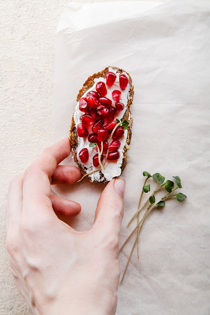 Hand hält Bruschetta belegt mit Frischkäse und Granatapfelkernen